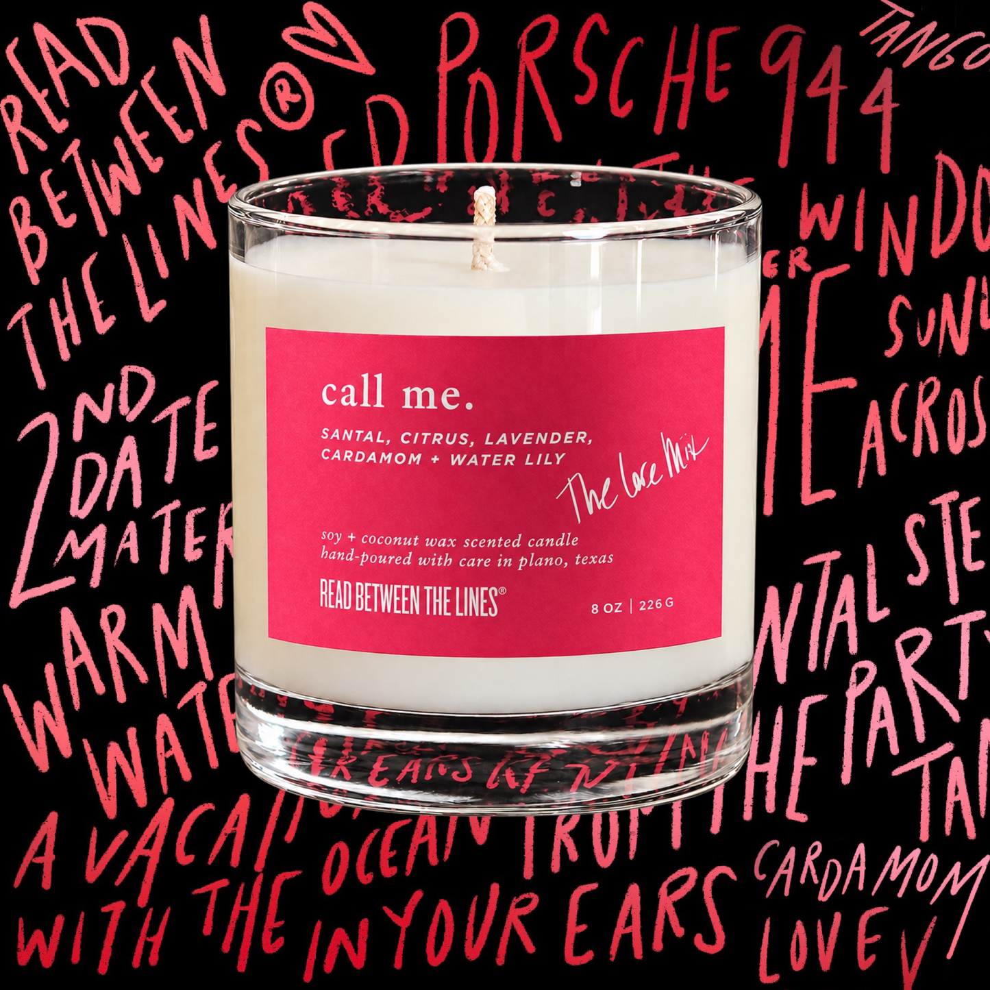 A clear glass jar candle with white wax and a bright pink label reading 'call me' and 'The Love of Me,' set against a black background covered in pink handwritten text.